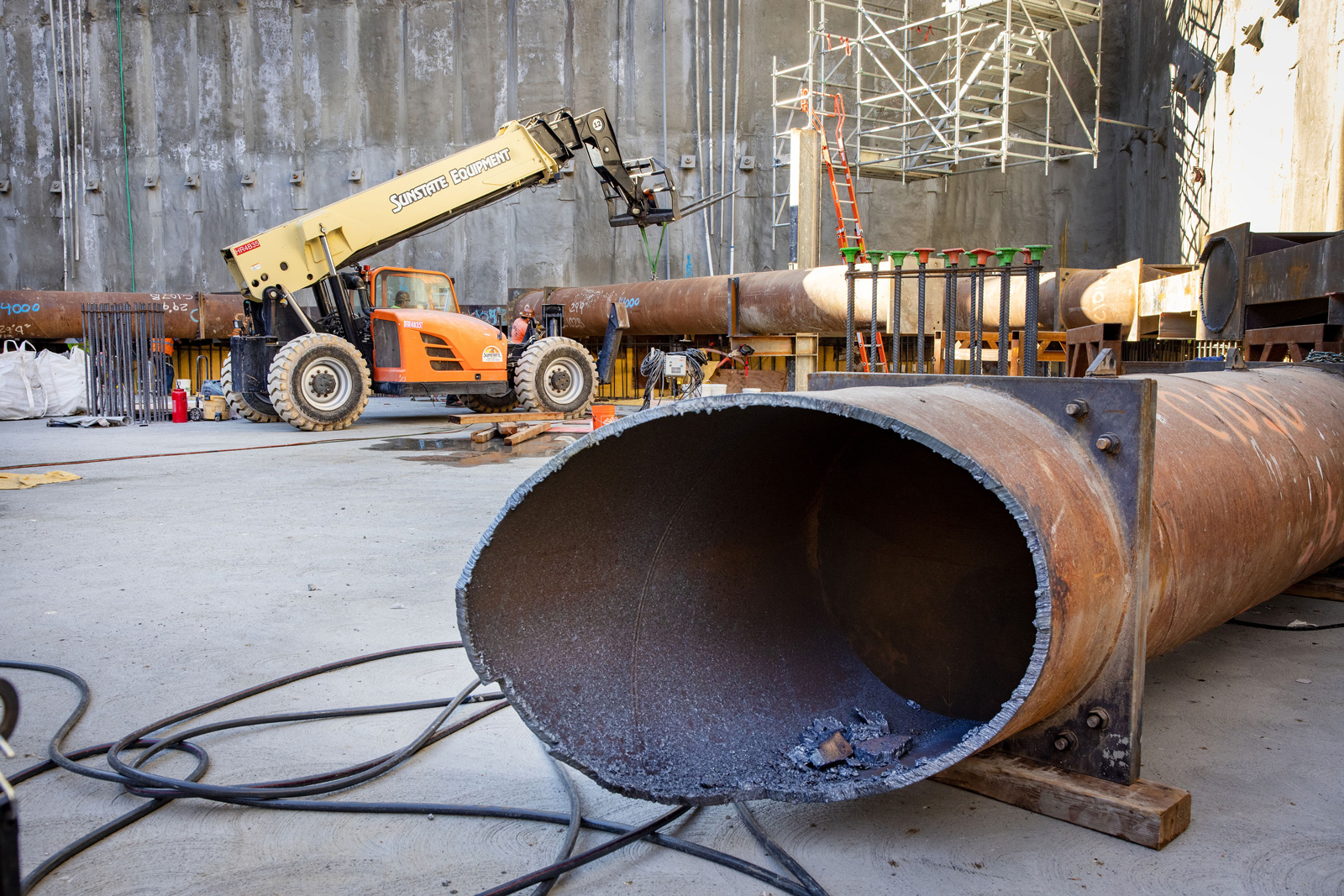 Underground construction of parking garage in San Mateo, with pipe in foreground and forklift