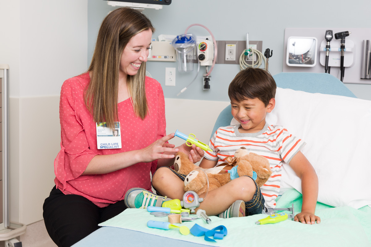 Hospital child life specialist in hospital emergency room working with young child to explain medical procedures